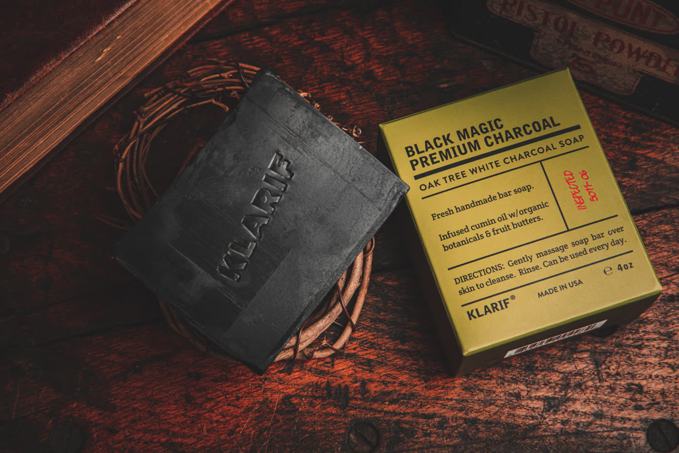 Klarif Black Magic charcoal soap bar beside its kraft box on dark wood